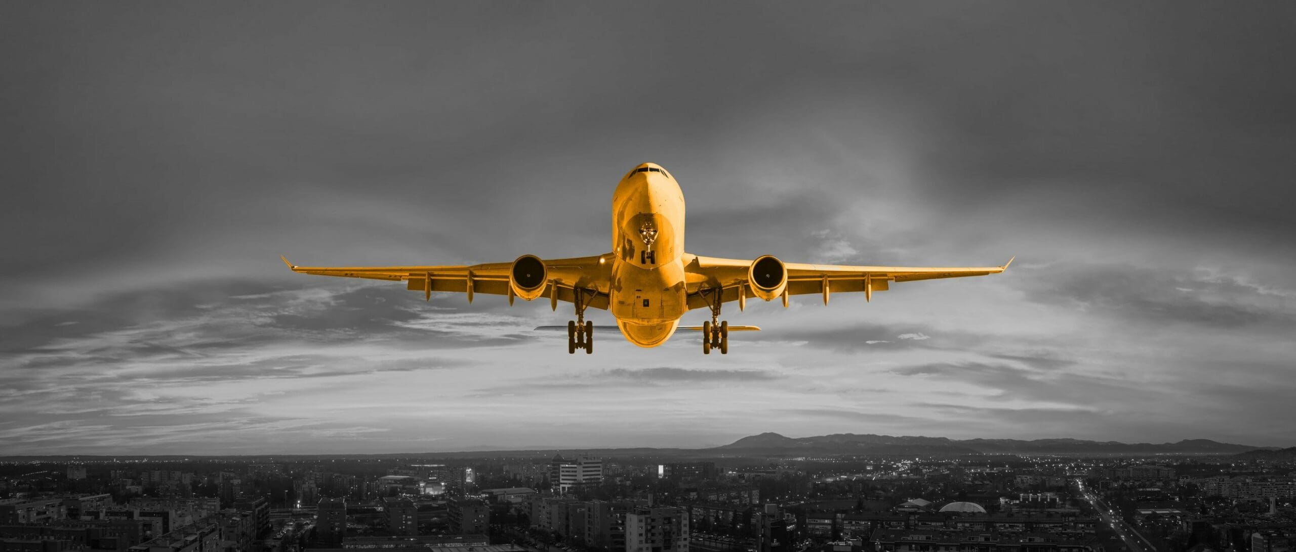 A black and white image with an orange aeroplane flying through the sky