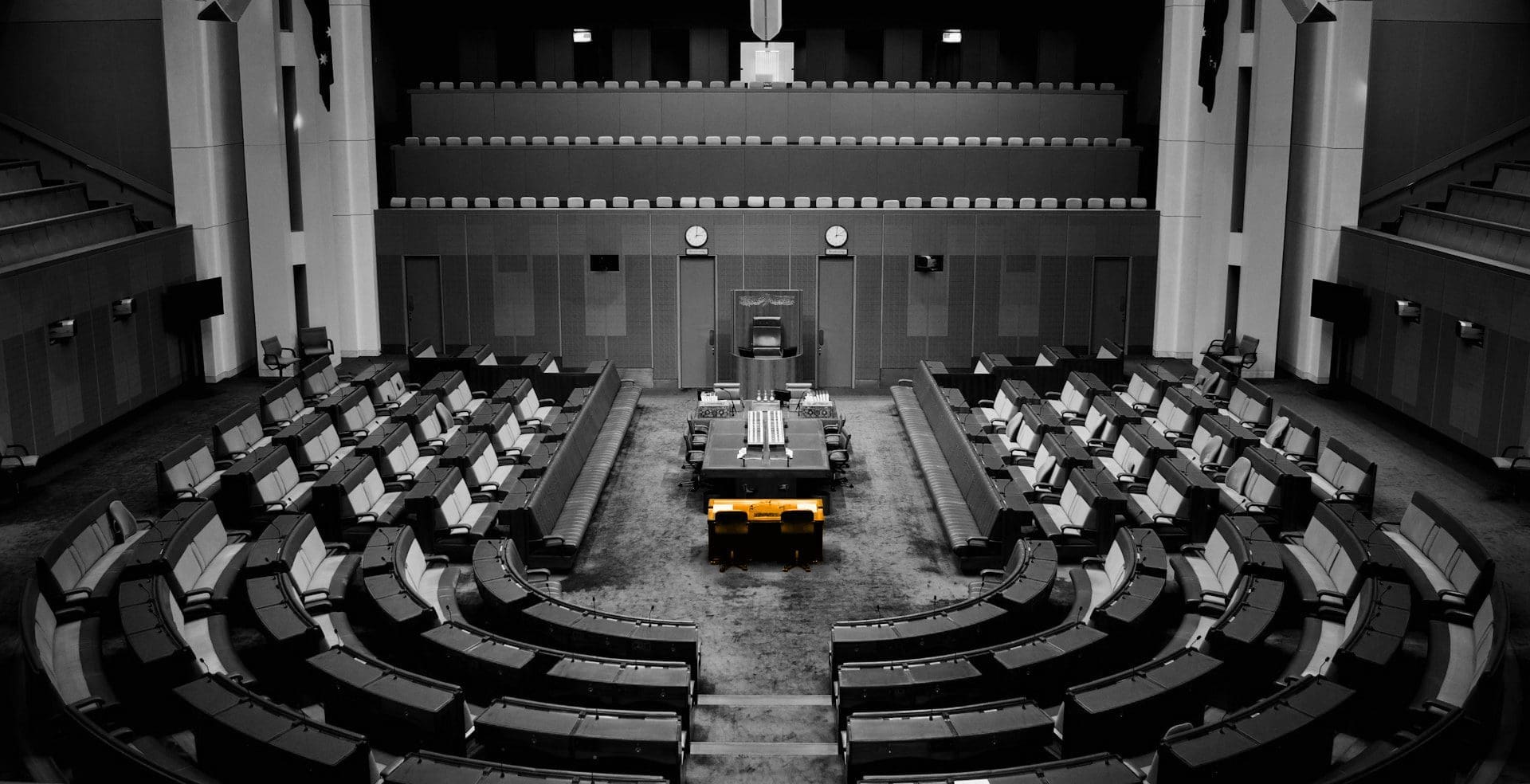 A black and white image of a governmental meeting, with an orange table in the middle