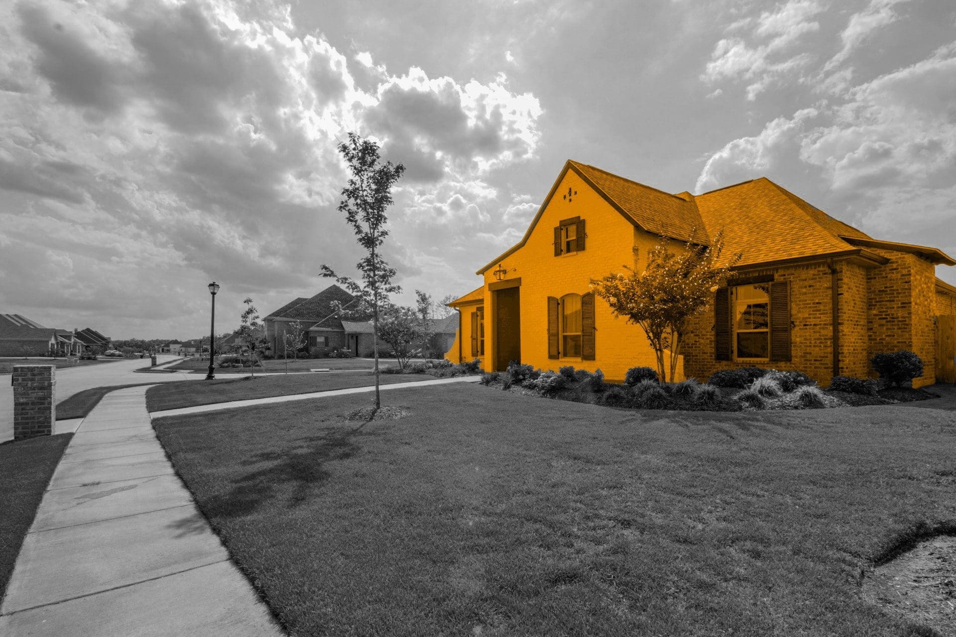 A black and white image of a street, with a orange house in the middle