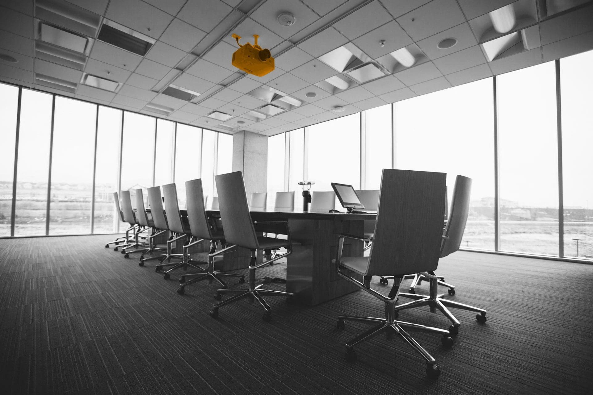 A black and white image of a meeting room with a orange projector on the ceiling