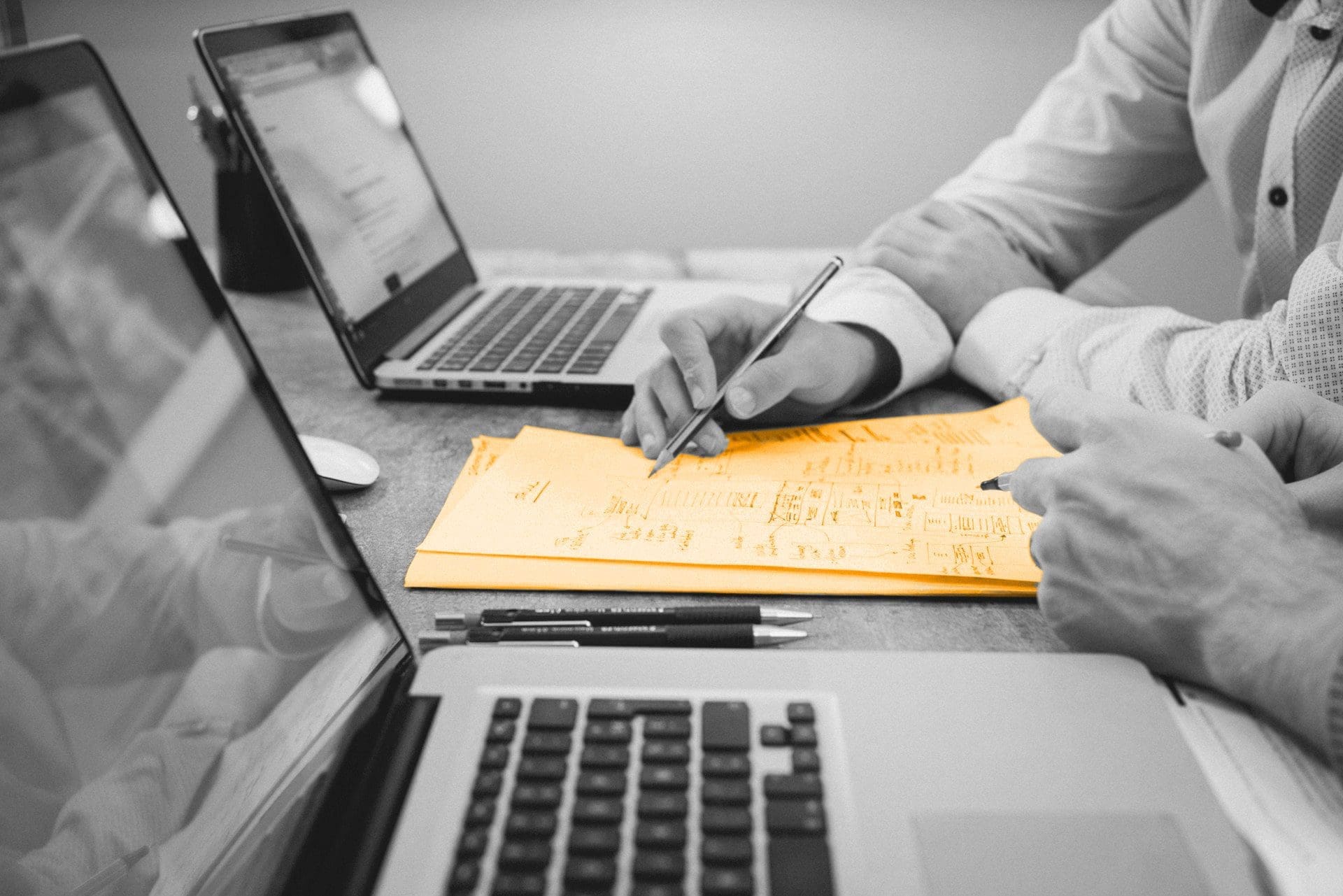 A black and white image of two people having a meeting, writing on a bunch of orange paper