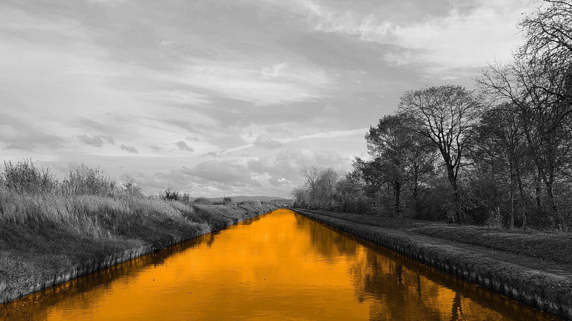 A black and white image of a field, with a orange river flowing through the middle of it