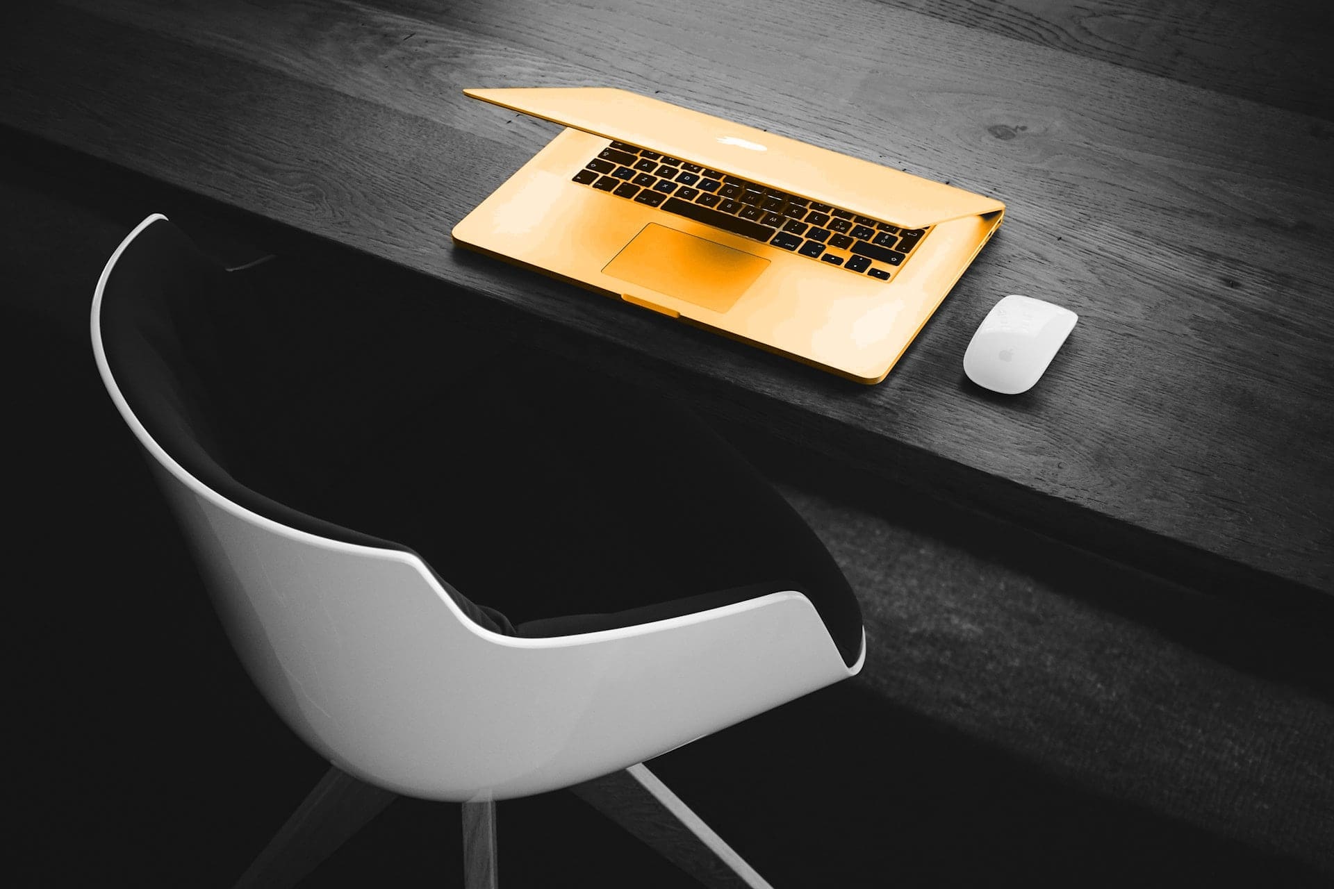 A black and white image of a chair and table, with a orange laptop sitting on the table