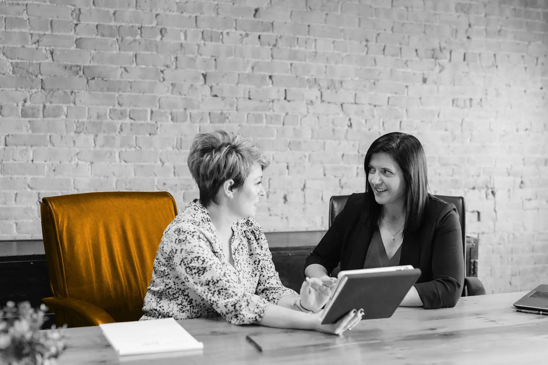 A black and white image of two woman having a meeting, with one of the woman sitting in an orange chair