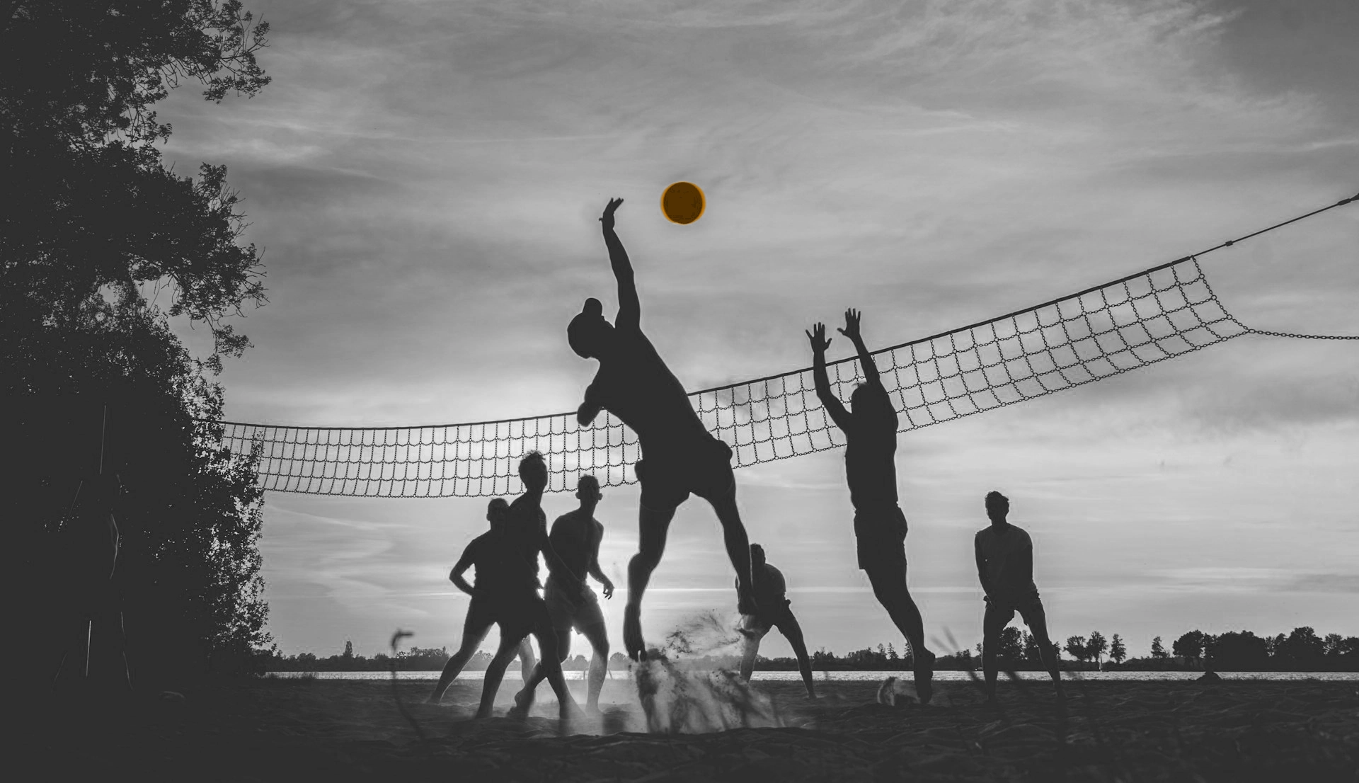 A black and white image of people playing volleyball. The ball is orange